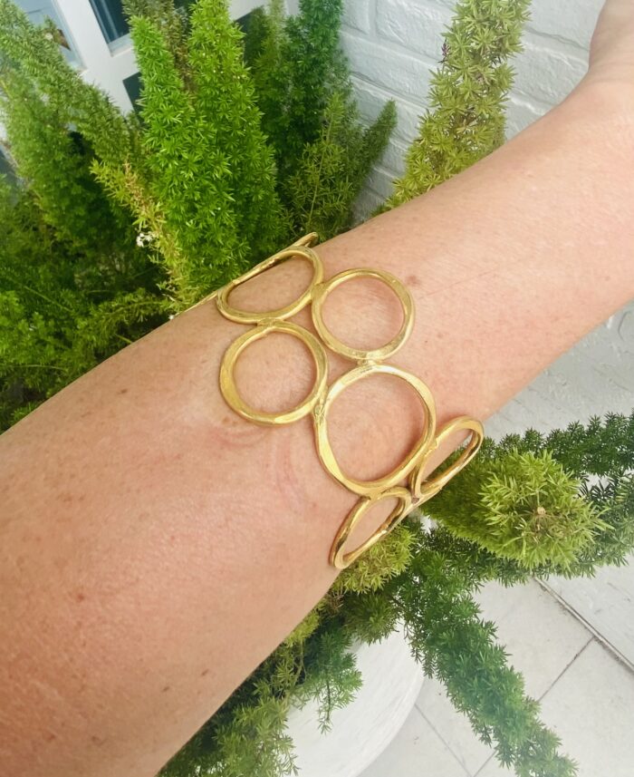 Brazalete rígido artesanal con círculos vacíos en latón dorado o plateado.