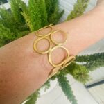 Brazalete rígido artesanal con círculos vacíos en latón dorado o plateado.