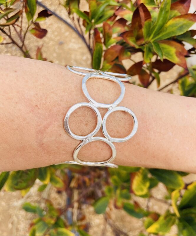Brazalete rígido artesanal con círculos vacíos en latón dorado o plateado.