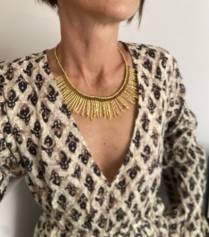 Collar artesanal dorado con diseño de rayos de sol y detalle de macramé burdeos, hecho a mano en India.