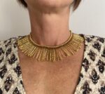 Collar artesanal dorado con diseño de rayos de sol y detalle de macramé burdeos, hecho a mano en India.