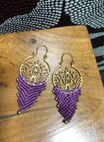 Pendientes de latón y macramé lila claro con diseño artesanal, sobre mesa.