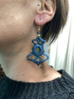 Pendientes de macramé azul oscuro con piedra central, usados por modelo.