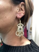 Pendientes de macramé blancos con piedra central y cuentas doradas, llevados por modelo.