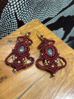 Pendientes de macramé rojos con piedra central y cuentas doradas sobre superficie de madera.