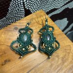 Pendientes de macramé verdes con piedra central y cuentas doradas sobre mesa.