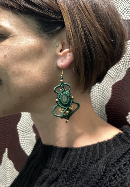 Pendientes de macramé verdes con piedra central y cuentas doradas, artesanales de India, llevados por una modelo.
