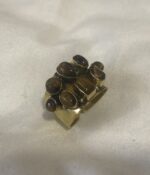 Anillo de latón ajustable con siete piedras Ojo de Tigre apoyado de lado sobre superficie clara.