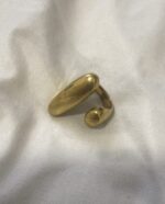 anillo abierto de latón dorado colocado de lado sobre superficie blanca