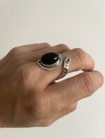 anillo ajustable con piedra negra colocado de lado sobre superficie neutra