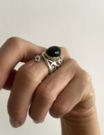 mano llevando anillo ajustable con piedra negra y base calada en baño de plata